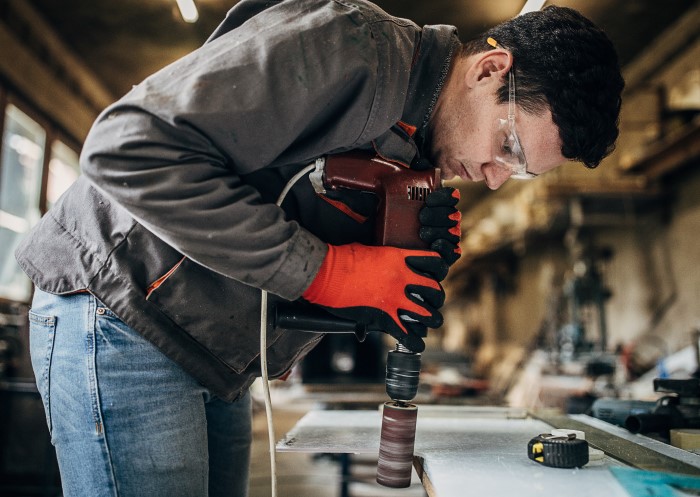 Mann mit Schutzbrille und Arbeitshandschuhen poliert Acrylglas in der Werkstatt