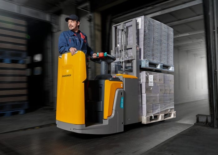 Lagermitarbeiter fährt mit Hochhubwagen befüllte Paletten zum Ausgang des Cross-Docking Zentrums
